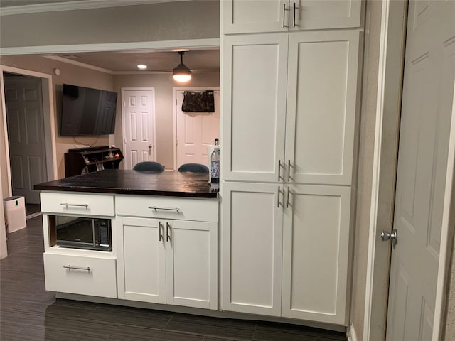kitchen featuring white cabinets, dark countertops, black microwave, a peninsula, and ornamental molding