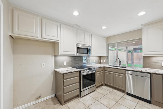 kitchen featuring light stone countertops, appliances with stainless steel finishes, a sink, recessed lighting, and tasteful backsplash
