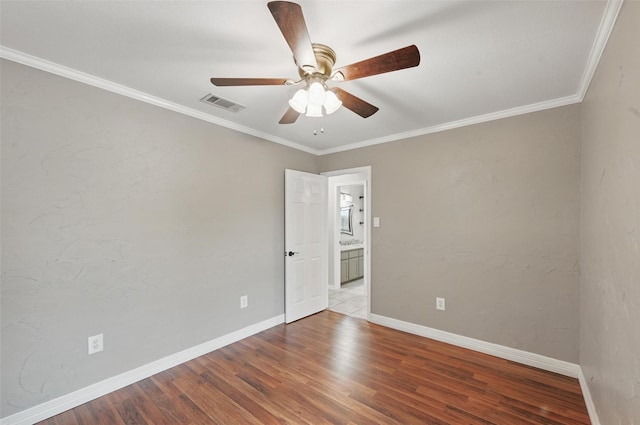 spare room with crown molding, a ceiling fan, baseboards, wood finished floors, and visible vents