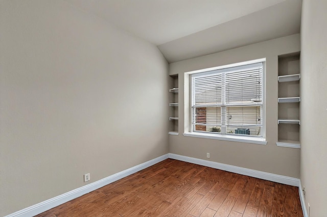 spare room featuring built in features, baseboards, vaulted ceiling, and wood finished floors