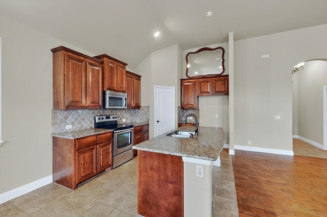 kitchen featuring light stone countertops, appliances with stainless steel finishes, a sink, arched walkways, and tasteful backsplash
