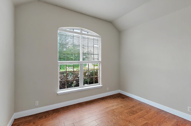spare room with baseboards, vaulted ceiling, and wood finished floors