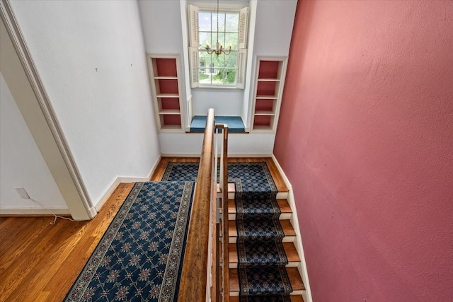 staircase with an inviting chandelier, baseboards, and wood finished floors