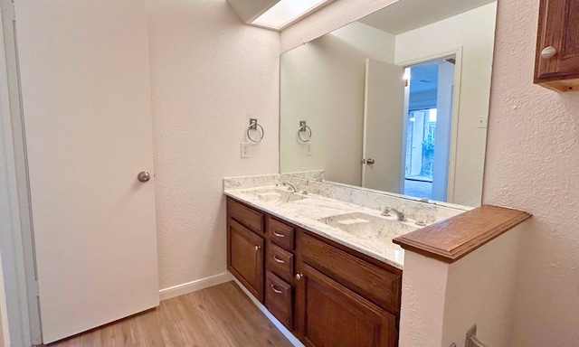 full bathroom featuring a sink, a textured wall, double vanity, and wood finished floors