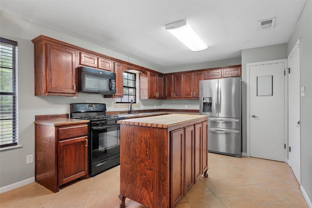 kitchen featuring a kitchen island, visible vents, a sink, black appliances, and butcher block counters