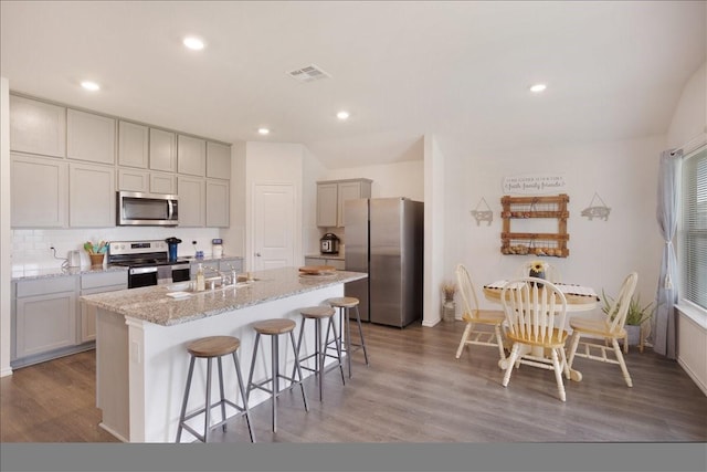 kitchen with a sink, light wood-style flooring, stainless steel appliances, a kitchen bar, and a center island with sink