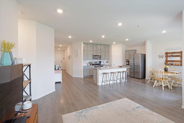 kitchen featuring appliances with stainless steel finishes, a kitchen breakfast bar, gray cabinets, wood finished floors, and a center island with sink