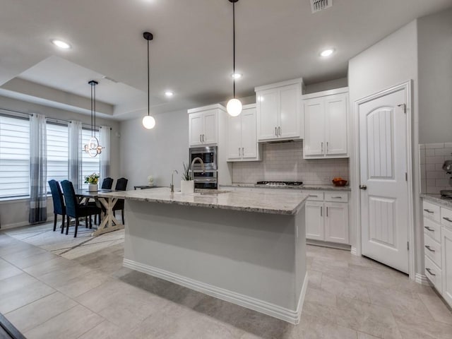 kitchen with an island with sink, decorative backsplash, stainless steel appliances, and white cabinets
