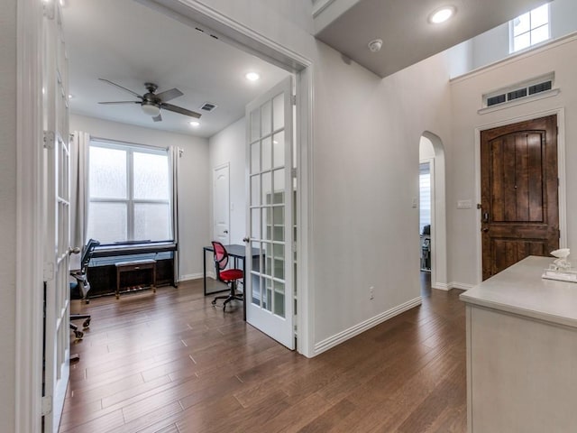 foyer entrance with arched walkways, a ceiling fan, visible vents, and dark wood-style floors