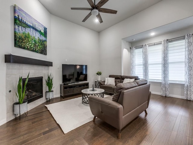 living area with baseboards, dark wood-style flooring, ceiling fan, and a tiled fireplace