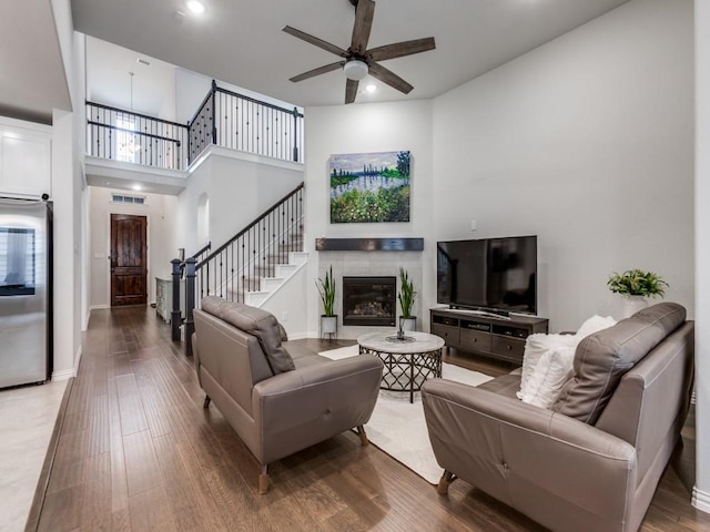 living area with a ceiling fan, a fireplace, wood finished floors, stairway, and baseboards