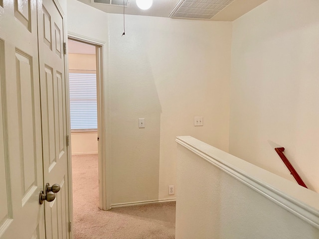 hall with light colored carpet, visible vents, and an upstairs landing