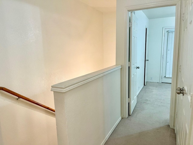 hallway with baseboards, an upstairs landing, and light carpet