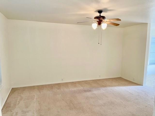 spare room featuring ceiling fan, light carpet, and baseboards