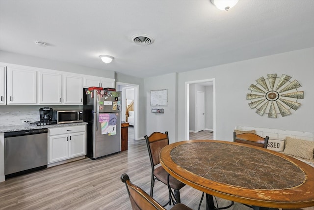 kitchen featuring white cabinets, light stone counters, stainless steel appliances, light wood-type flooring, and visible vents