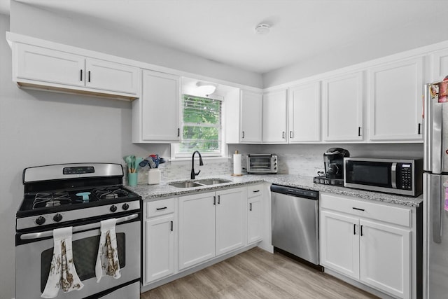 kitchen with appliances with stainless steel finishes, a sink, light stone counters, white cabinets, and light wood-style flooring