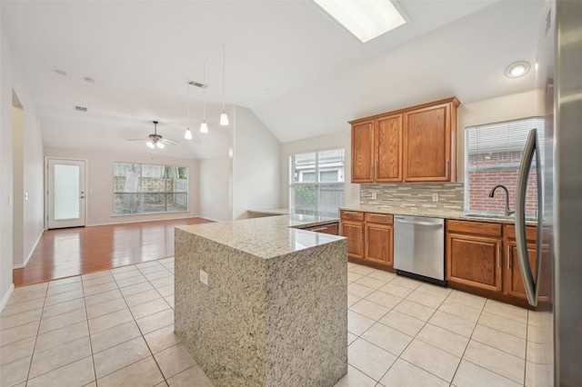 kitchen featuring brown cabinetry, decorative backsplash, light tile patterned floors, stainless steel dishwasher, and vaulted ceiling