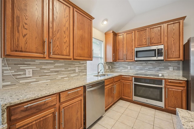 kitchen with brown cabinetry, lofted ceiling, a sink, appliances with stainless steel finishes, and light tile patterned floors