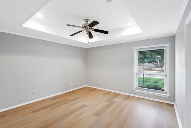 empty room featuring light wood-type flooring, baseboards, and a tray ceiling