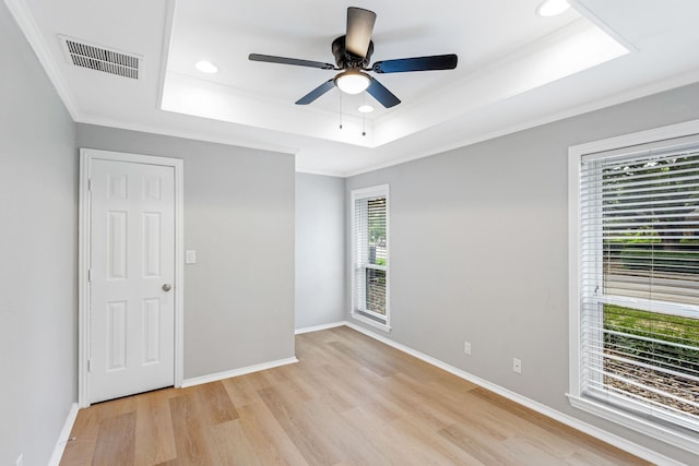 empty room with a ceiling fan, visible vents, ornamental molding, a tray ceiling, and light wood-style flooring