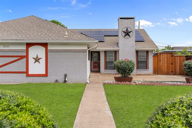 view of front of house with roof with shingles, solar panels, a front lawn, and brick siding