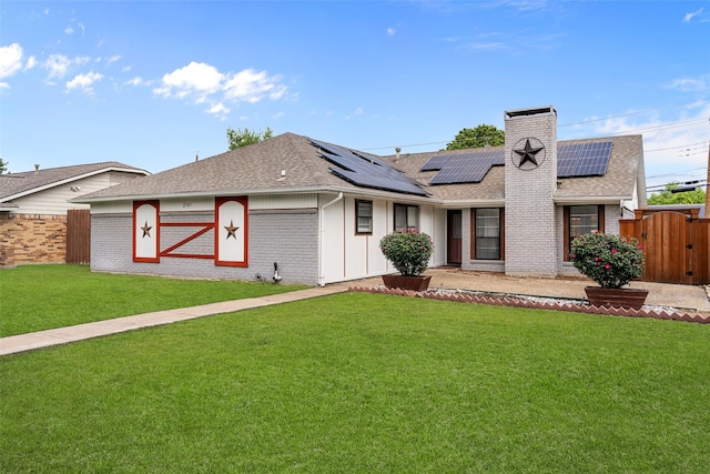 ranch-style home with brick siding, a shingled roof, roof mounted solar panels, and a front yard