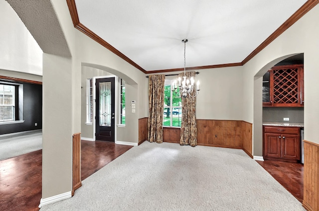 interior space featuring carpet flooring, arched walkways, wood walls, a wainscoted wall, and ornamental molding
