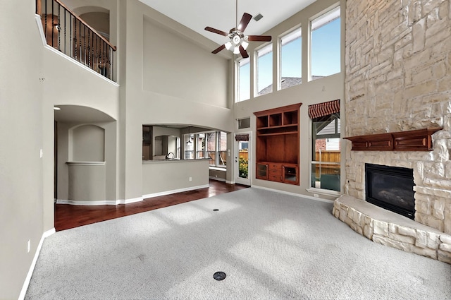 unfurnished living room featuring ceiling fan, a stone fireplace, baseboards, a high ceiling, and carpet