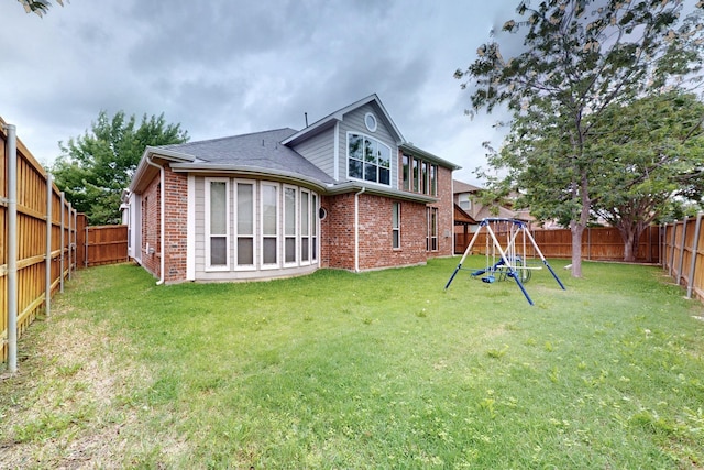 rear view of house with brick siding, a fenced backyard, a playground, and a lawn