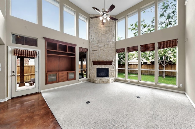 unfurnished living room featuring a wealth of natural light, ceiling fan, a fireplace, and a high ceiling