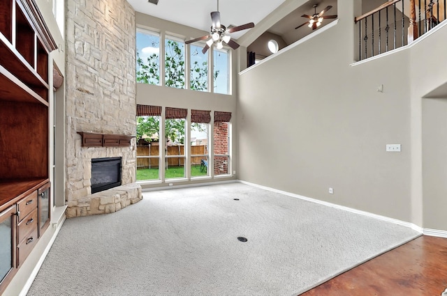 unfurnished living room with a ceiling fan, a fireplace, baseboards, carpet floors, and a high ceiling