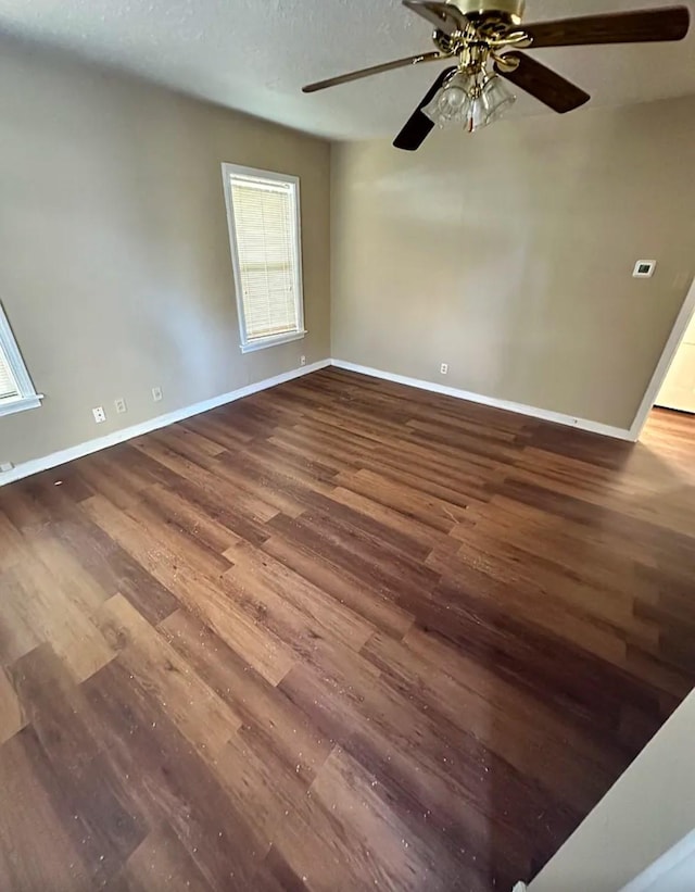 spare room featuring baseboards, ceiling fan, wood finished floors, and a wealth of natural light