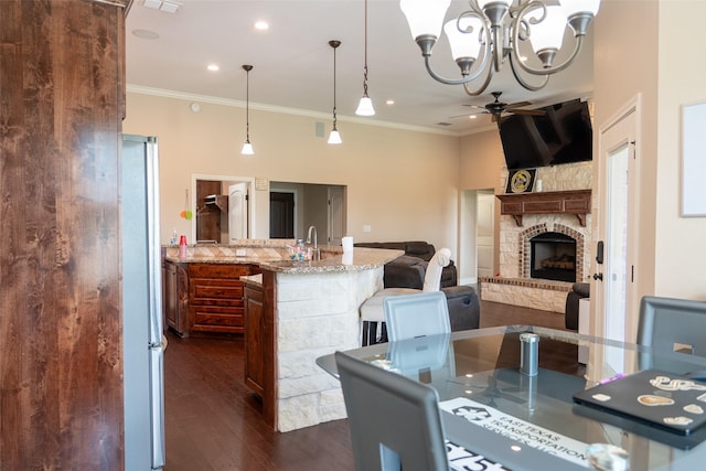 dining area with crown molding, a fireplace with raised hearth, a chandelier, and dark wood finished floors