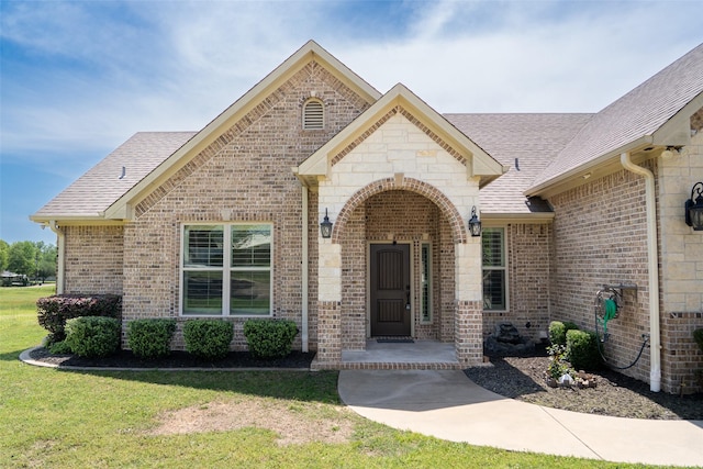 doorway to property featuring roof with shingles, stone siding, a lawn, and brick siding