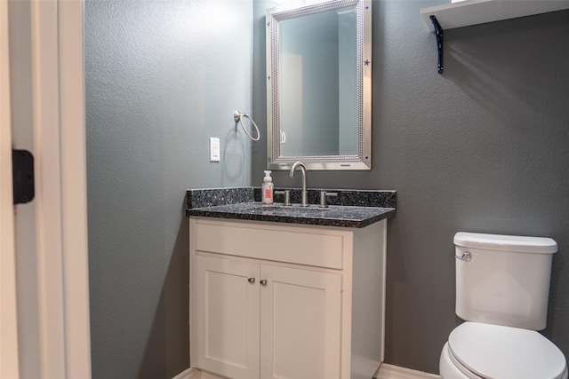 half bathroom featuring vanity, a textured wall, and toilet
