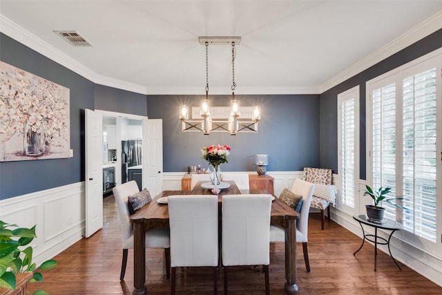 dining area with visible vents, wood finished floors, a chandelier, ornamental molding, and a decorative wall