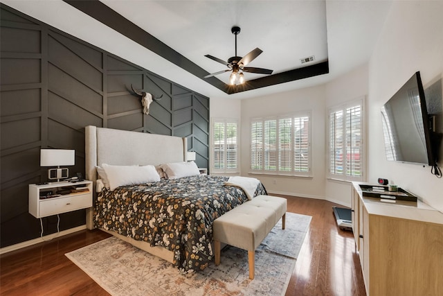 bedroom with visible vents, wood finished floors, a raised ceiling, baseboards, and a decorative wall