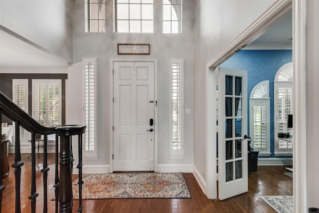 entryway with baseboards, a towering ceiling, crown molding, and wood finished floors