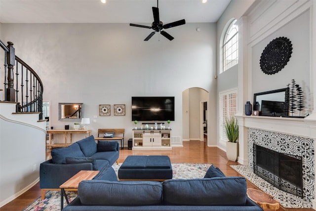 living room with a ceiling fan, wood finished floors, a high ceiling, stairway, and arched walkways