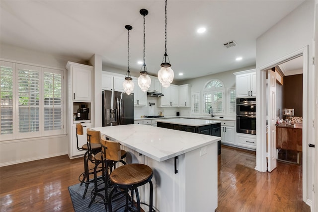 kitchen with a kitchen island, visible vents, stainless steel appliances, dark wood-style floors, and under cabinet range hood
