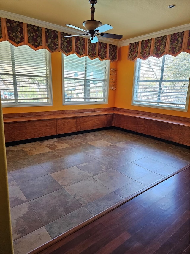 unfurnished dining area with wainscoting, a ceiling fan, and ornamental molding