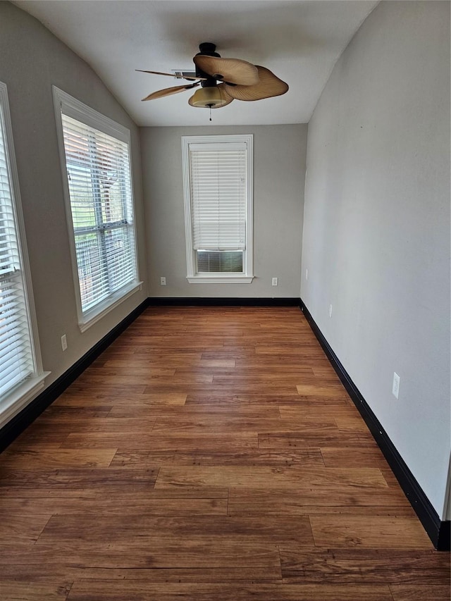 spare room featuring a ceiling fan, baseboards, dark wood-style floors, and lofted ceiling