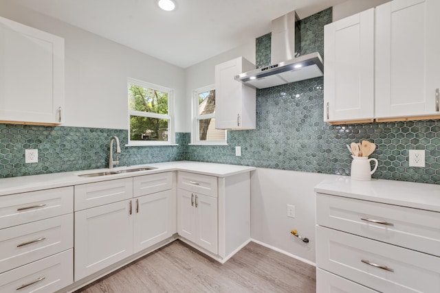 kitchen with light wood-type flooring, a sink, wall chimney exhaust hood, and light countertops