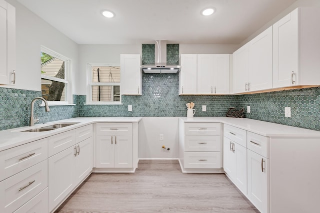 kitchen featuring wall chimney range hood, light wood finished floors, a sink, and white cabinetry