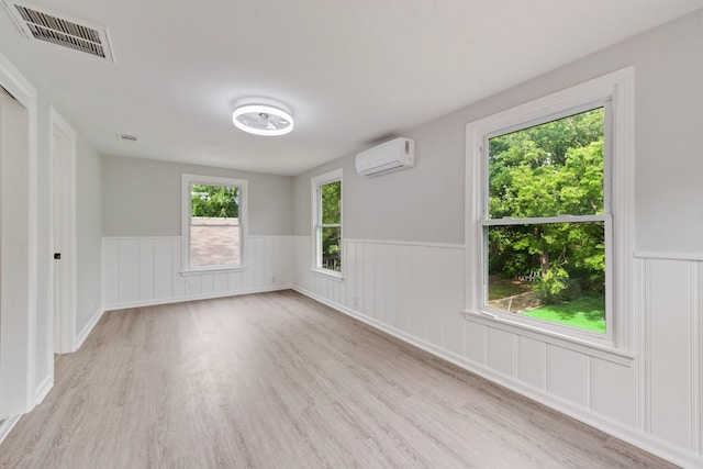 unfurnished room featuring plenty of natural light, a wainscoted wall, a wall unit AC, wood finished floors, and visible vents