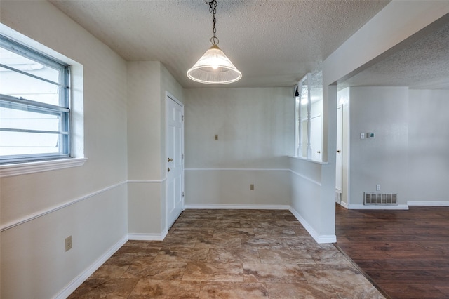unfurnished dining area featuring visible vents, a textured ceiling, and baseboards