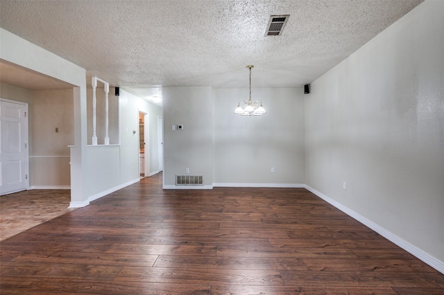 spare room with a textured ceiling, visible vents, an inviting chandelier, and hardwood / wood-style flooring