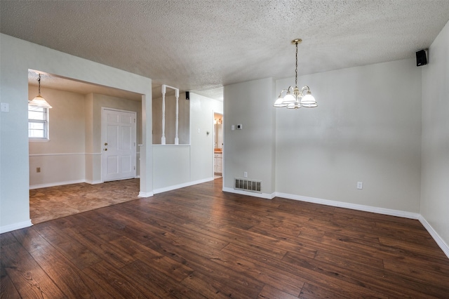 unfurnished room with a notable chandelier, dark wood finished floors, a textured ceiling, and visible vents