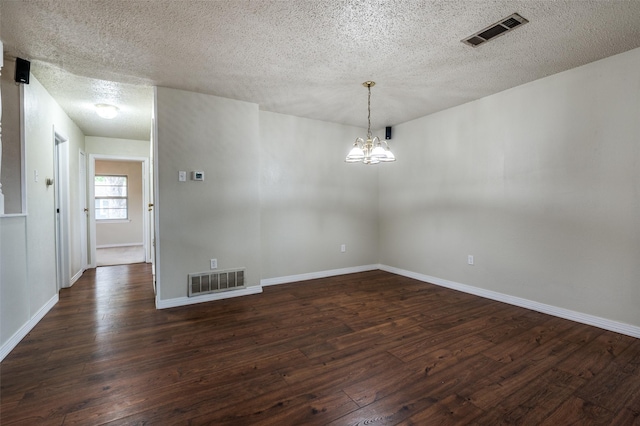 empty room featuring visible vents, a textured ceiling, dark wood-style flooring, and a chandelier