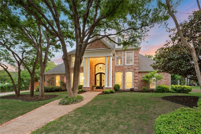 greek revival inspired property with roof with shingles, a front lawn, and brick siding